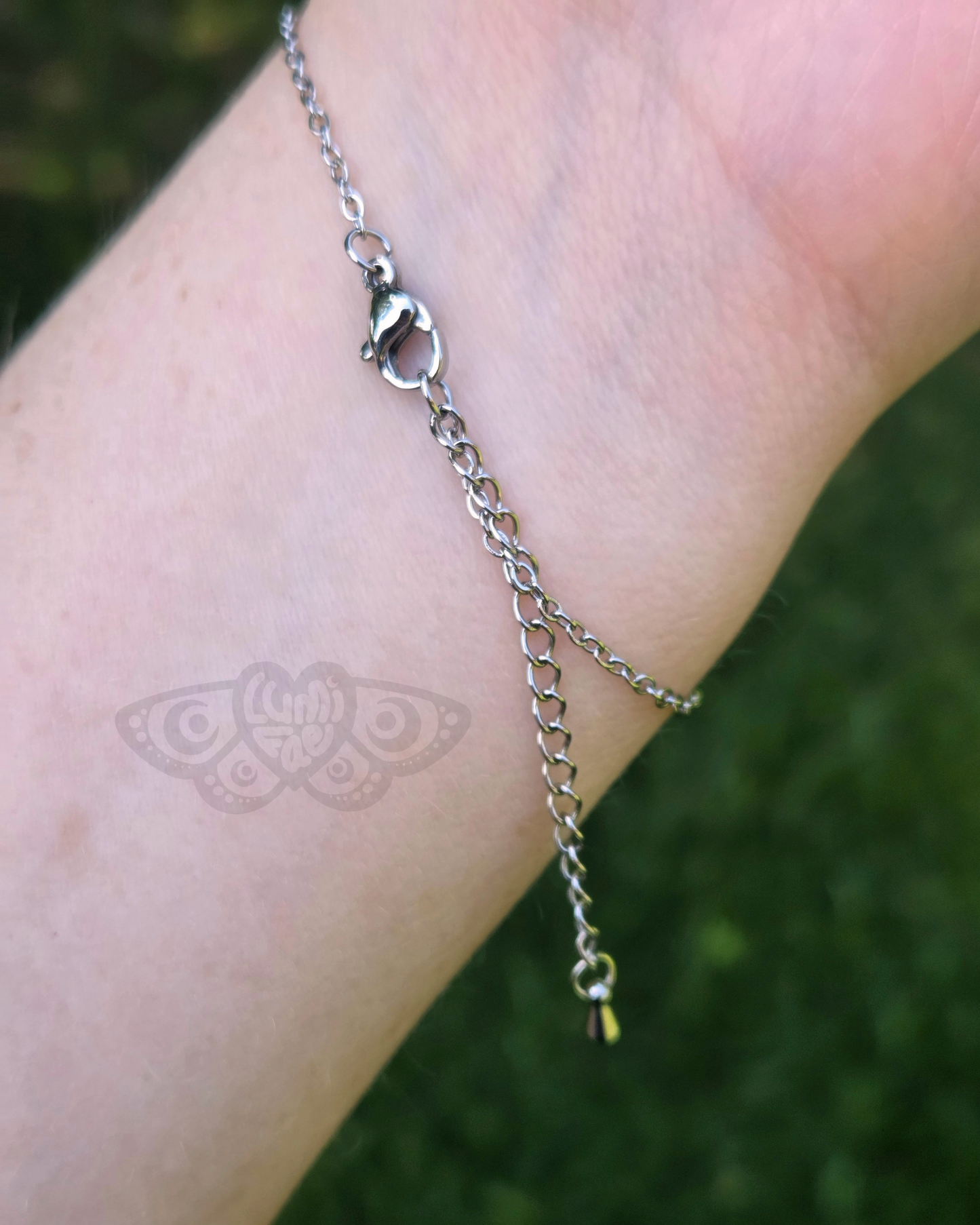 Back of ladybug bracelet shows a silver chain worn on a wrist against a grassy background