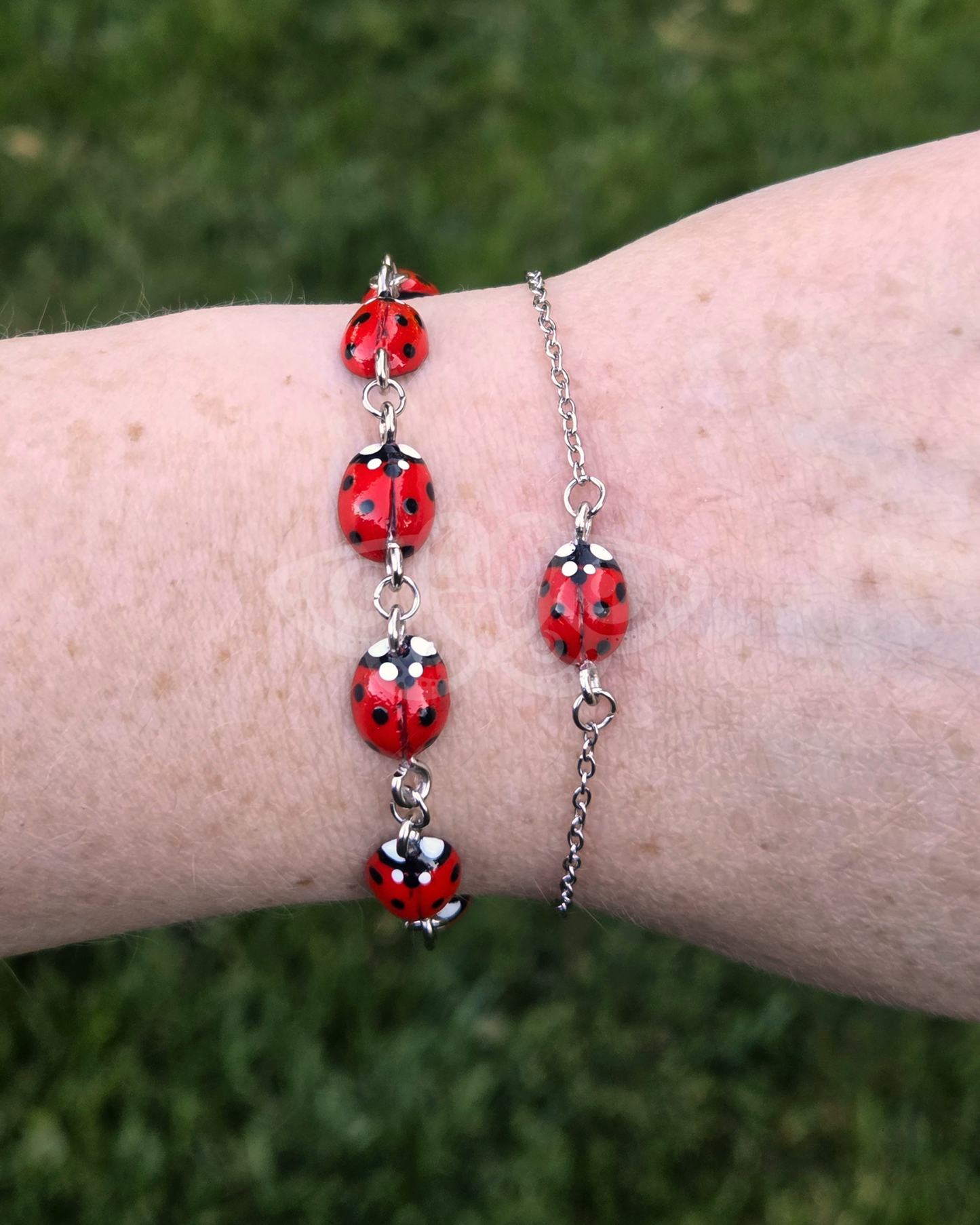 Two Ladybug Bracelets on a wrist against a grass background, one bracelet has many ladybugs, the other bracelet has one ladybug