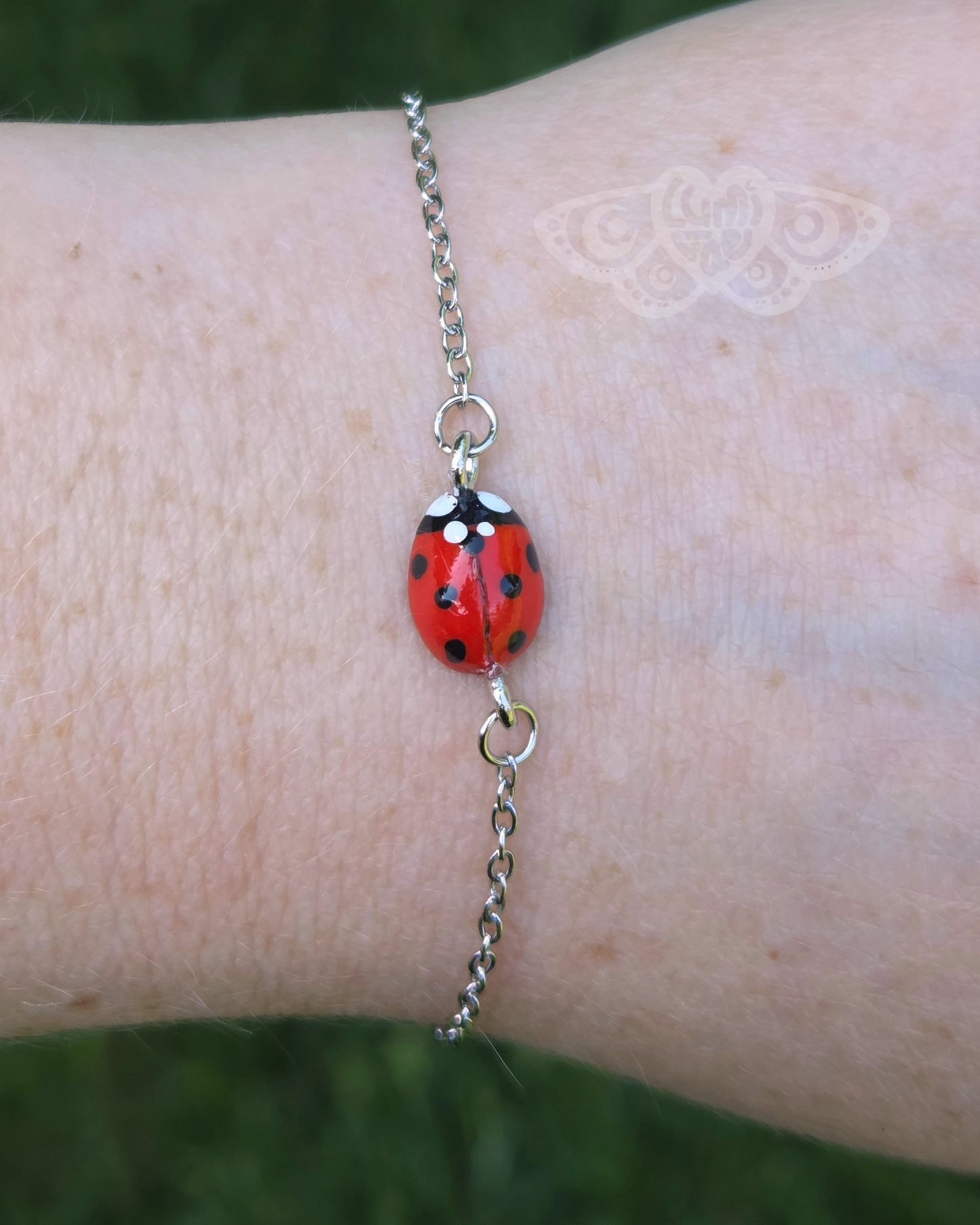 Close up of a bracelet featuring a realistic red ladybug worn on a wrist against a grassy background