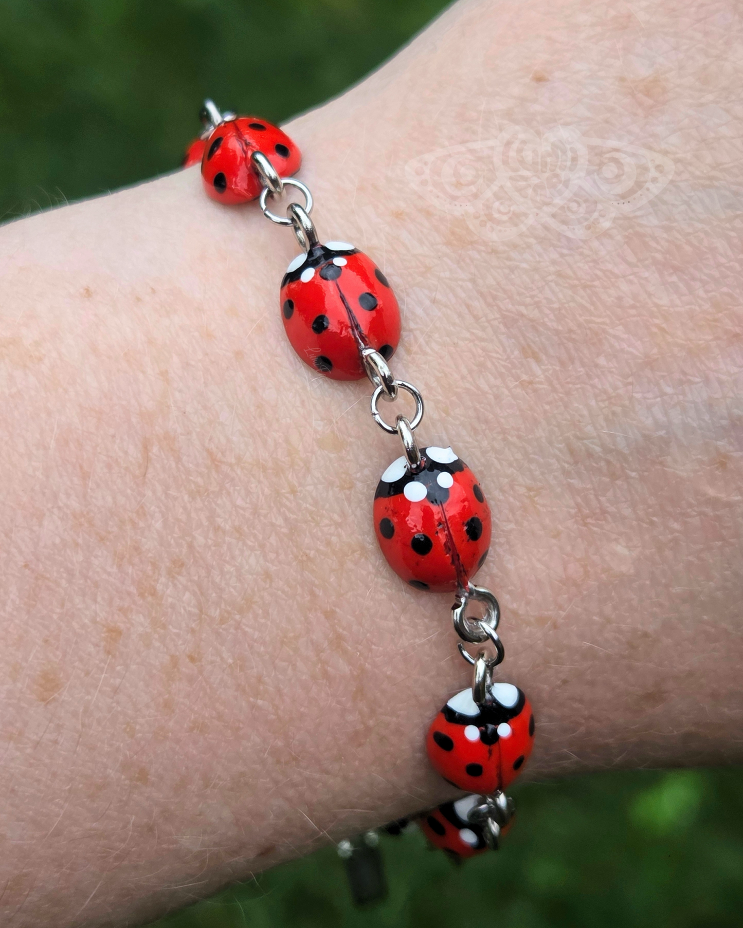 Bracelet with ladybugs on a wrist against a blurred green background