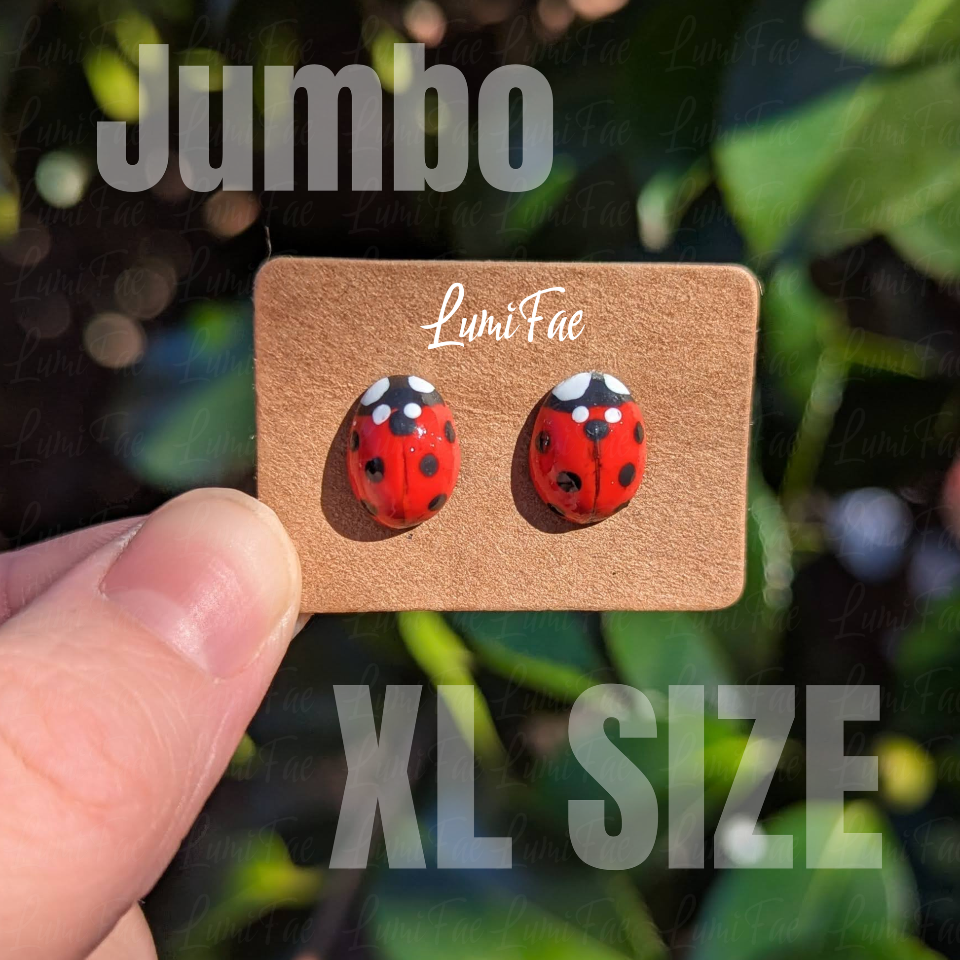 Red ladybug earrings on a LumiFae jewelry card with 'Jumbo XL Size' text, held against a blurred green leaves background.