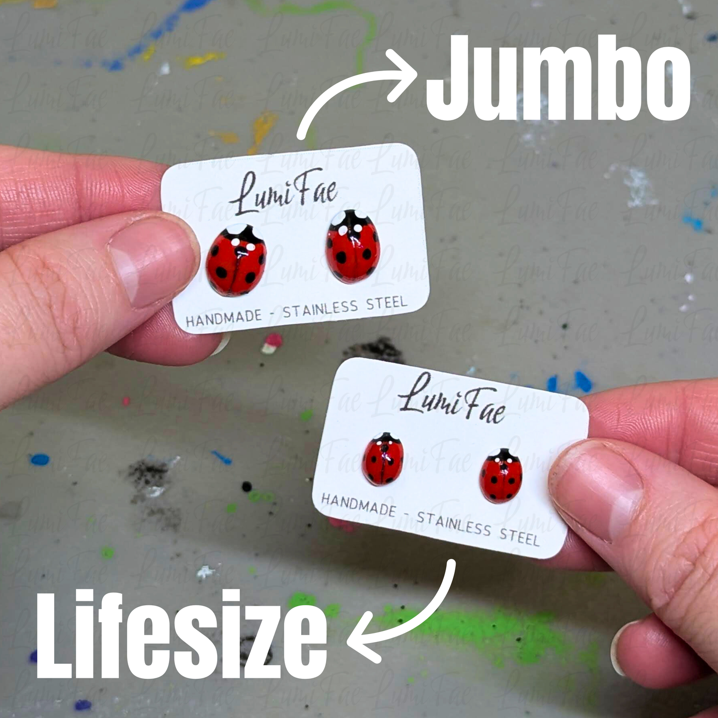 A large pair and a small pair of ladybug earrings on earring cards held by a hand with 'Jumbo' and 'Lifesize' text denoting each pairs’ size.