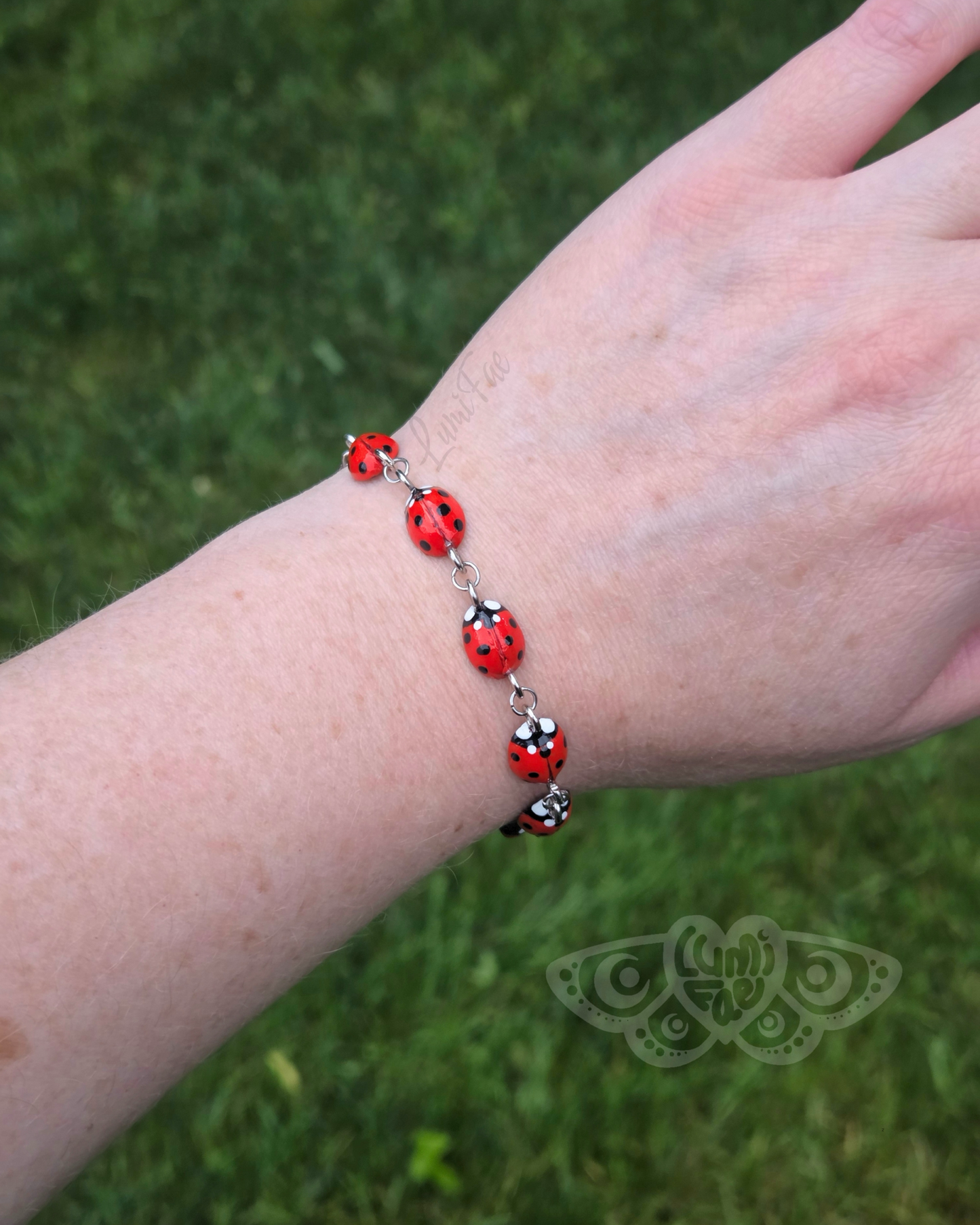Bracelet with red ladybugs on a wrist against a grassy background