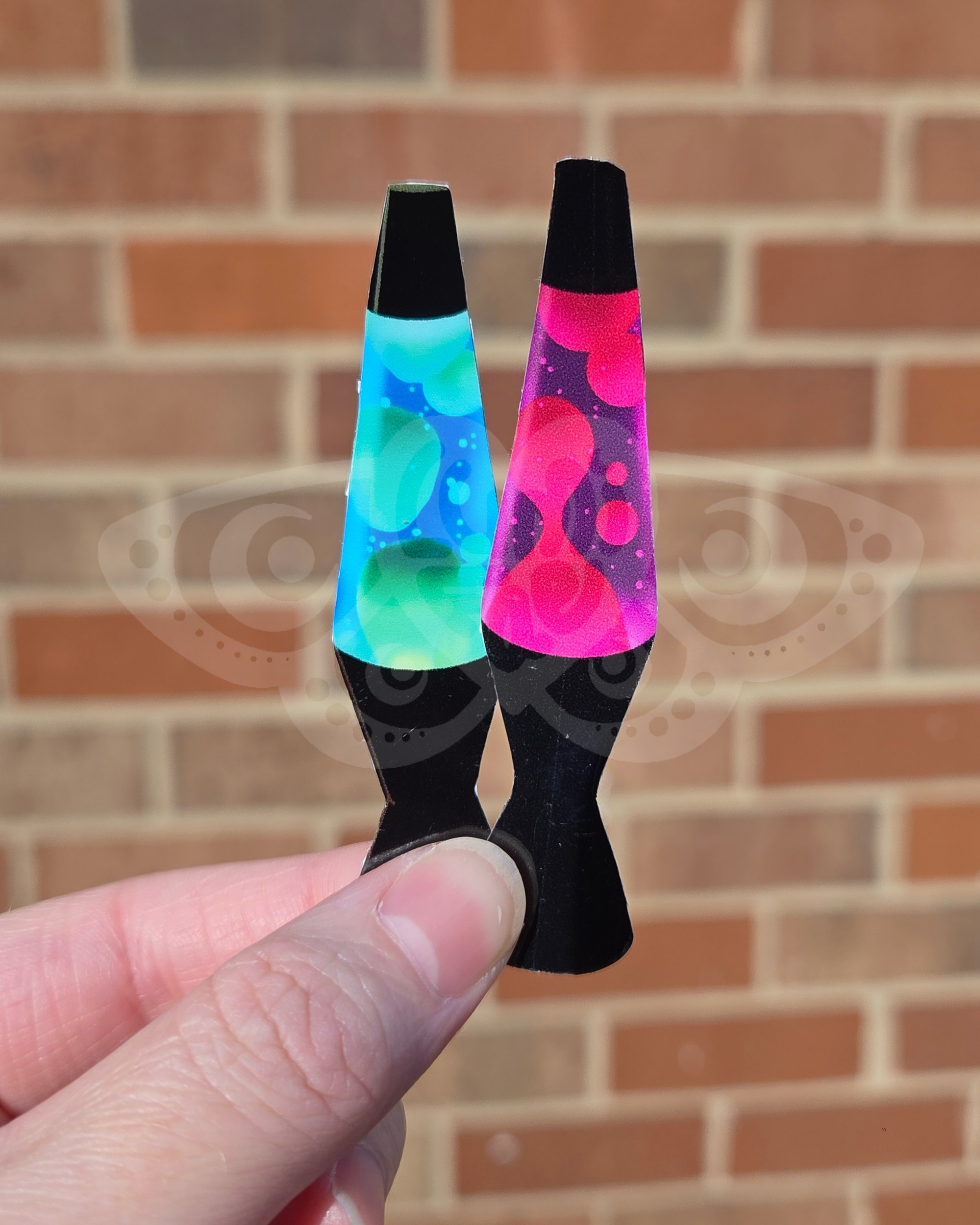 Two small lava lamps srickers held against a brick wall.
