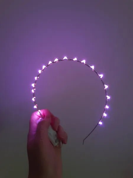 Pink LED  Headband held by a hand and glowing against a white background 